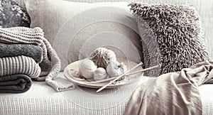 Vintage wooden knitting needles and threads for knitting on a cozy sofa with pillows and sweaters