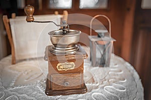 Vintage wooden manual coffee grinder, small decorative lantern and a newsstand on a round table with a white embroidered