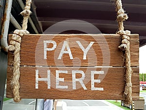 Vintage wooden sign to indicate cashier location. Pay Here written on planks.