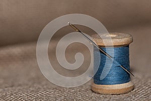 vintage wooden spool with blue threads and needle on a textured light Braun color background