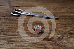 on a vintage wooden table lie old iron scissors  sewing bobbin with red thread  the concept of harmony of two parts  needlework