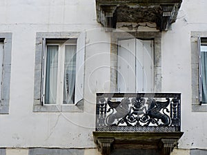 Vintage worn balcony with black metallic ornate on the beige weathered facade downtown in France.