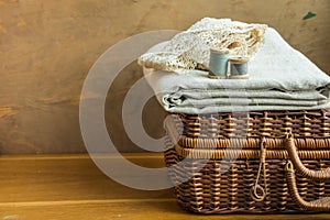 Vintage woven rattan crafts and sewing supply box, wooden spools, rolls of lace, folded linen fabric, aged wood background, hobby