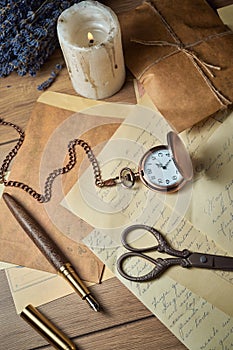 Vintage writing utensils on a wooden table, old watch, papers, letters, envelopes and scissors