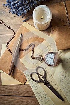 Vintage writing utensils on a wooden table, old watch, papers, letters, envelopes and scissors