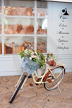 Vintage yellow bike with a basket with flowers stands near the cafe of a bakery against the background of the wooden blue house. S