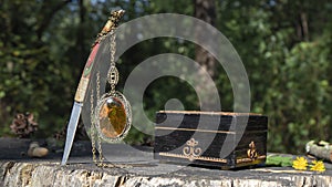 A vintage yellow glowing amber pendant hangs from a knife stuck in an old tree stump in the forest.