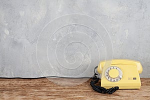 Vintage yellow rotary dial telephone on wooden table in front gray concrete background