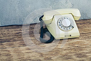 Vintage yellow rotary dial telephone on wooden table in front gray concrete background