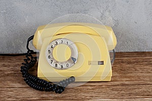 Vintage yellow rotary dial telephone on wooden table in front gray concrete background