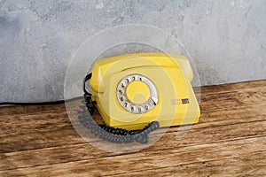 Vintage yellow rotary dial telephone on wooden table in front gray concrete background