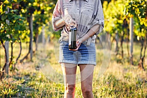 Vintner holding red wine bottle and drinking glass in vineyard