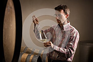 Vintner taking sample of white wine in cellar.