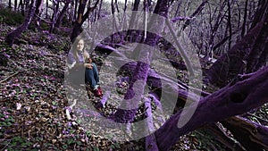 Violet fairytale forest. Beautiful girl in a lilac jacket sits in a fabulous lilac forest and looks at the flower in her