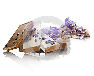 Violet flavored chocolate pieces, with violets and chocolate shavings, on a white plain background