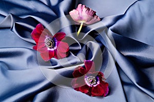 Violet flowers lie on a blue shiny silk wavy fabric.