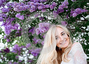 Violet flowers of lilac hang over the smiling blonde lady