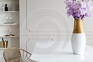 Violet flowers on white table in simple dining room interior with wall with molding. Real photo