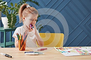 Violet marker in the mouth. Cute little girl in art school draws her first paintings