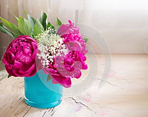 Violet peony flowers in blue vase on wooden table closeup