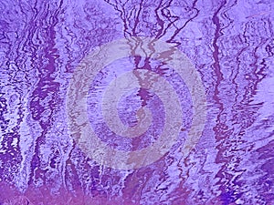 Violet rippling water surface with reflections of bare trees and sky