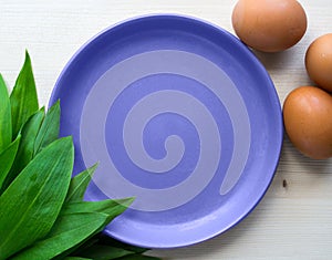 Violet saucer among ramson and eggs on bright wooden background