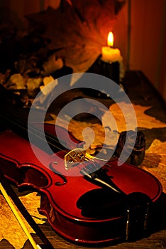 Violin, burning candle and autumn leaves on the table