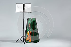 Violin in case and note stand with music sheets on grey. Space for text