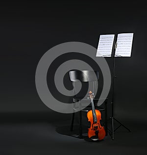 Violin, chair and note stand with music sheets on black background.