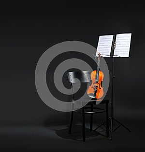 Violin, chair and note stand with music sheets on black background.