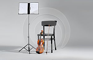 Violin, chair and note stand with music sheets on grey