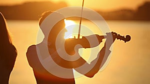 Violin duet man and woman play violin on nature at the sunset on the lake