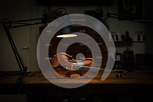 Violin after the luthiery under the lamp in the dark workshop