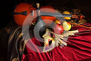 Violin next to a bottle of old wine and ripe fruits on the table, red velvet tablecloth, theatrical mask, Dutch still life