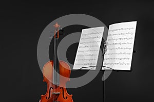 Violin and note stand with music sheets on black
