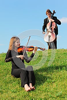 Violinist and violoncellist play against sky