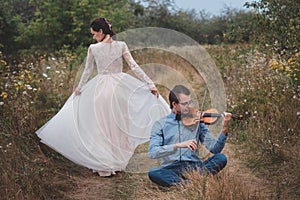 Violinist and woman in white dress , young man plays on the violin the background nature