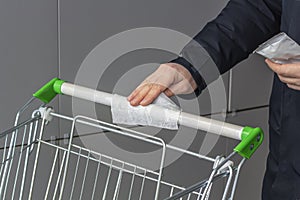 Viral disease prevention concept. Man wipes down a handle of public shopping cart with a disinfecting moist towelette in mall or