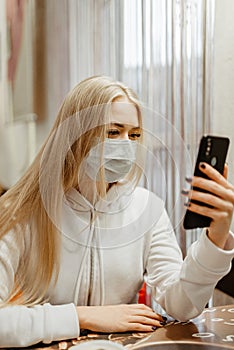 Viral mask. European blonde girl in flu mask for prevention. Looking at the phone