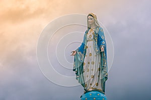 Virgin Mary statue at Catholic church with sunlight in cloudy day background.