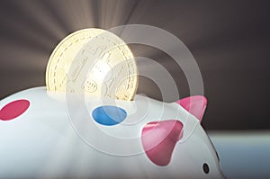 Golden bitcoin on and piggy bank over gently lit dark background and light ray