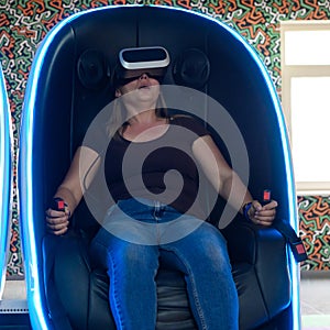 Virtual reality attraction, virtual glasses and entertainment in playrooms for children. A woman sits in a 5d neon chair