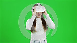 Virtual Reality concept. Front view of a young asian woman looking around, wearing a white shirt and a VR headset, greenscreen
