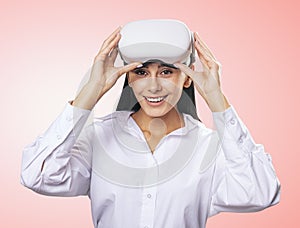 Virtual reality concept: smiled girl in light shirt with white VR glasses on her head on light pink background, close up