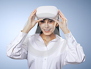 Virtual reality concept: smiled woman in light shirt with VR glasses on her head on light blue background, close up