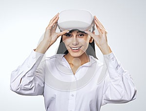 Virtual reality concept: smiled woman in light shirt with VR glasses on her head on light grey background, close up