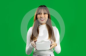 Virtual Reality concept. Young asian woman in white shirt holding a white VR headset, greenscreen