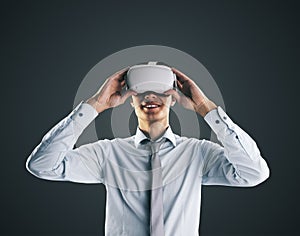 Virtual reality concept with young businessman gets new emotions in VR glasses on his head on abstract black background, close up