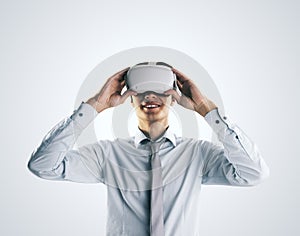 Virtual reality concept with young businessman gets new emotions in VR glasses on his head on abstract light grey background,