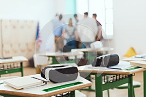 Virtual reality headsets on tables with teacher and high school students standing behind